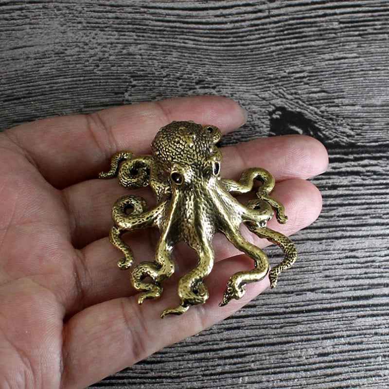 Gold octopus pendant held in a hand against a wooden background