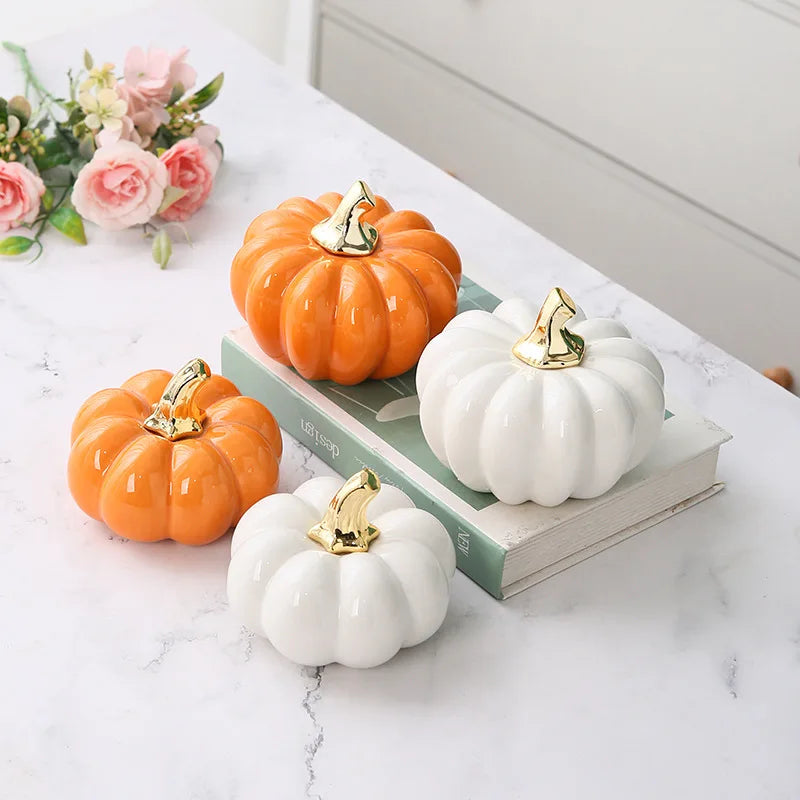 Four ceramic pumpkins, two orange and two white, with gold stems, arranged on a book and a marble surface.