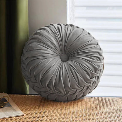 Round gray pillow on a textured surface with a window in the background