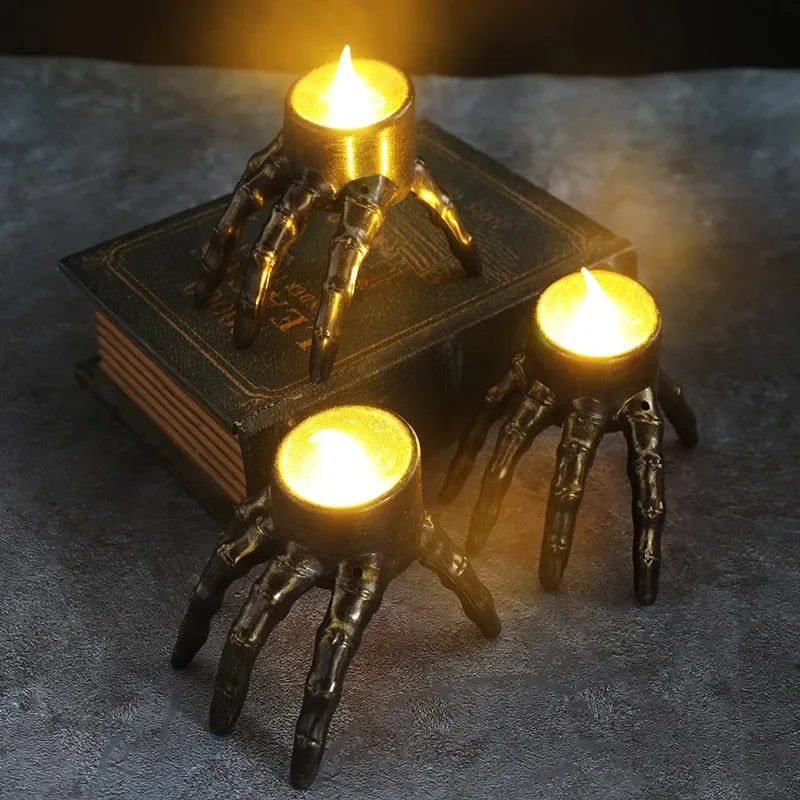 Three skeleton hand candle holders with lit candles, one is on top of a book.