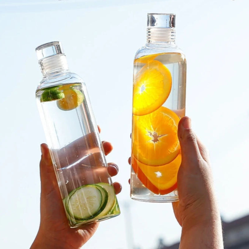 Two hands holding glass bottles with fruit-infused water.