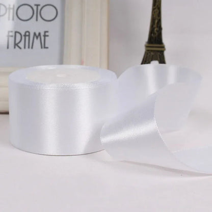 White satin ribbon roll on a white surface with a blurred photo frame and Eiffel Tower in the background.