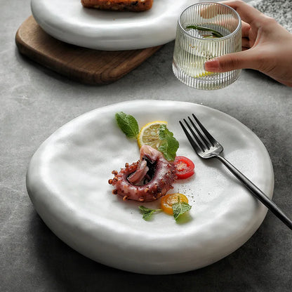 White plate with octopus dish, lemon, and tomatoes on a gray surface.