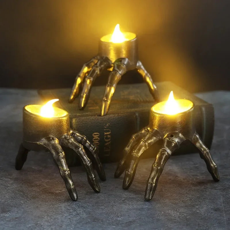 Three candles in skeletal hand holders, one on top of a book.