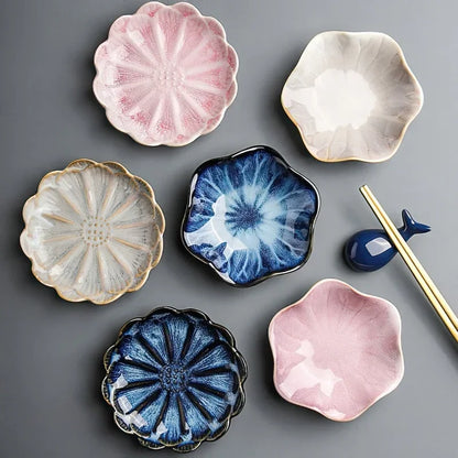 A group of small, flower-shaped condiment or sauce dishes in various colors, with a pair of chopsticks and a whale-shaped chopstick rest.