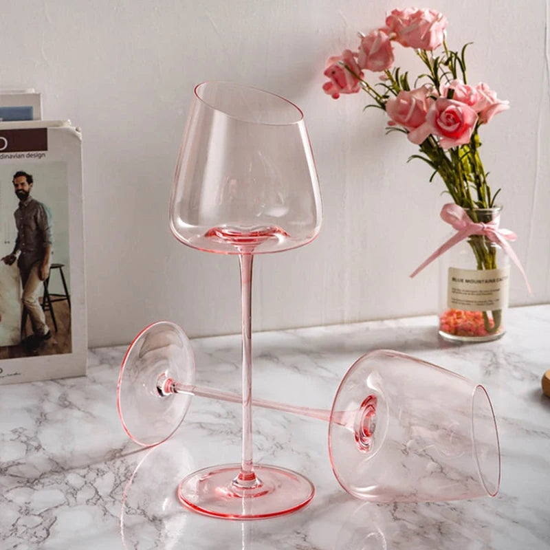 Two clear wine glasses with pink stems and an angled rim, one standing and one lying down.