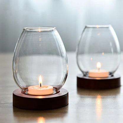 A pair of elegant glass candle holders with wooden bases, each containing a lit tealight candle. The soft, diffused lighting creates a calm and minimalist atmosphere, perfect for home decor.