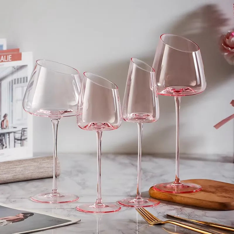 Four empty, clear wine glasses with pink stems and an angled rim.