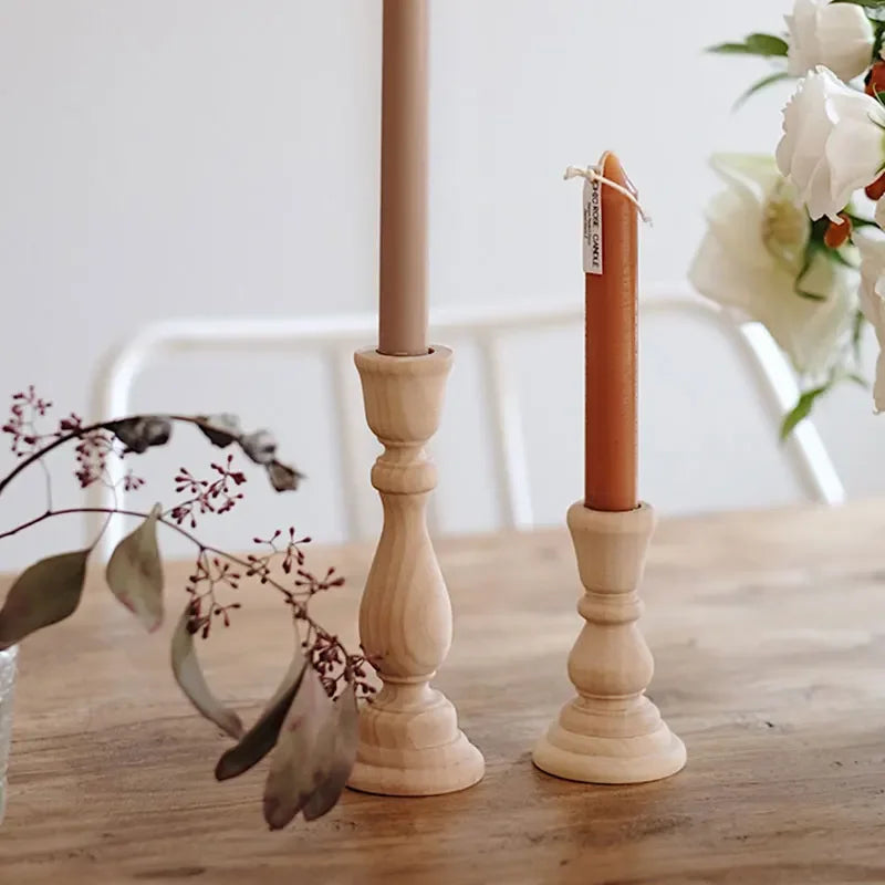 Two light wood candlestick holders, one taller than the other, hold brown and orange tapered candles on a wooden table.