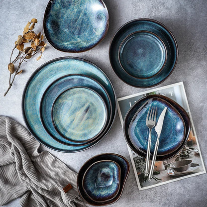 Set of blue ceramic plates and bowls on a gray surface with a magazine underneath.
