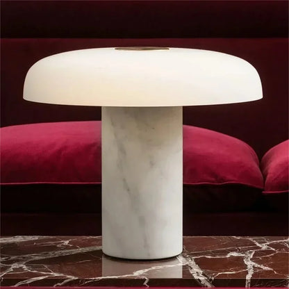 A modern mushroom-shaped table lamp with a white marble base and a white dome shade, sitting on a red marble table.