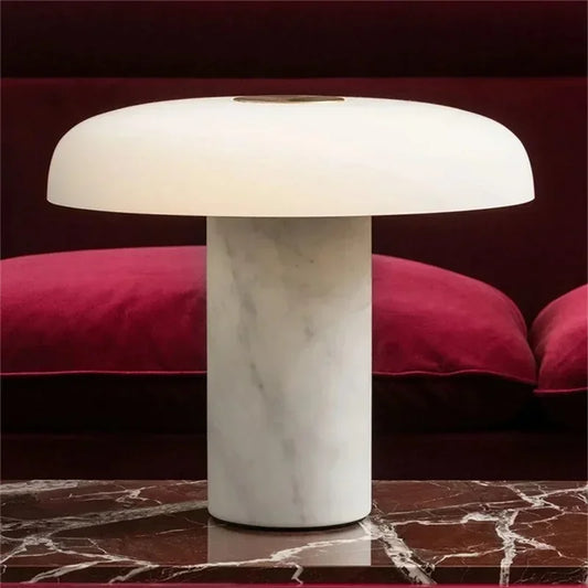 A modern mushroom-shaped table lamp with a white marble base and a white dome shade, sitting on a red marble table.