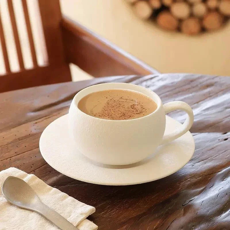 A white textured coffee cup with a drink and cinnamon, on a matching saucer, with a spoon and napkin.