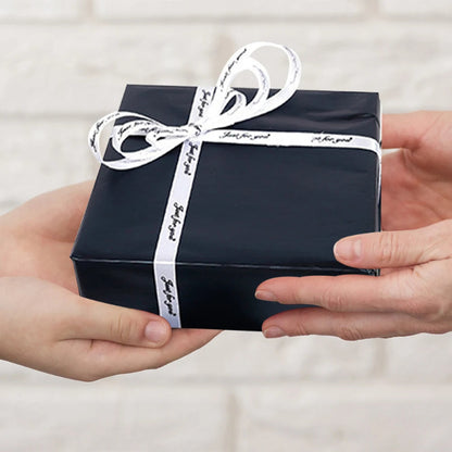 Black gift box with white ribbon held by two hands against a neutral background