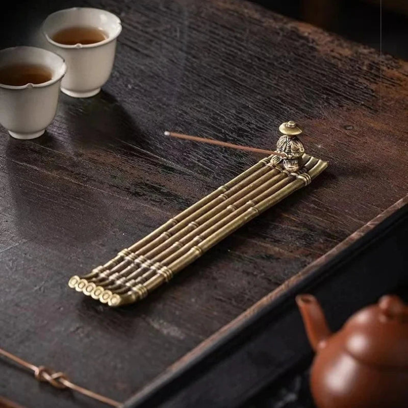 Decorative incense holder on a wooden surface with tea cups and a teapot.