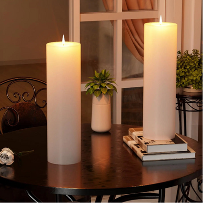 Two flameless pillar candles illuminate a dark room with warm light. A white rose and potted plant accent the candles.