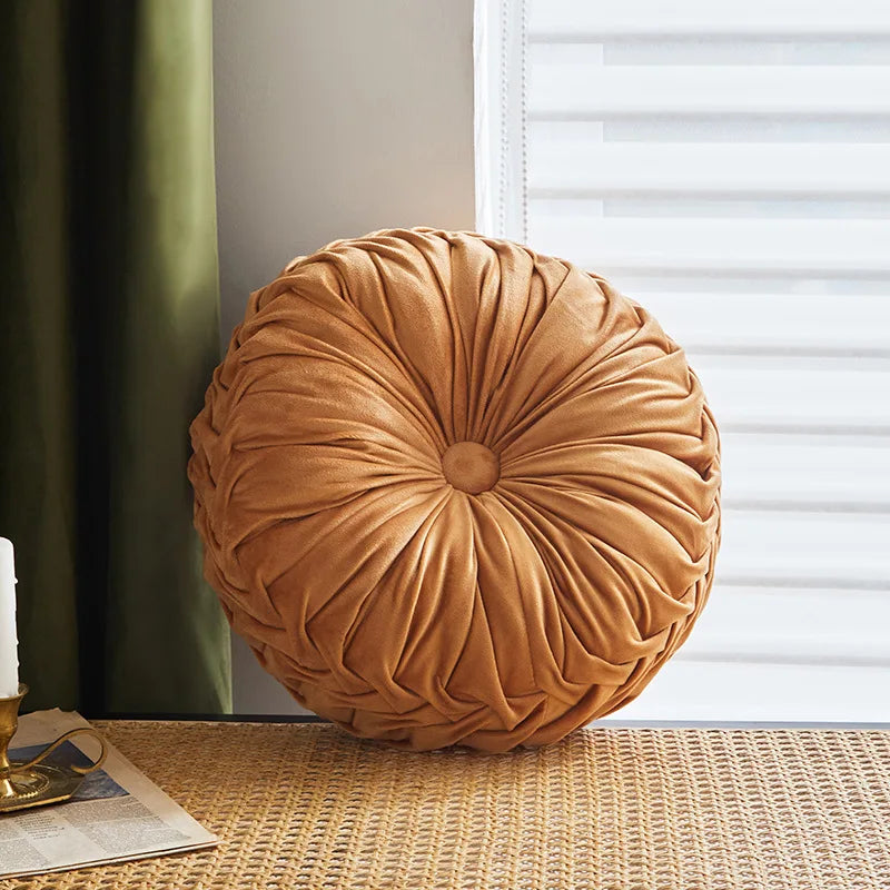 Round brown pillow on a textured surface with a window and curtain in the background