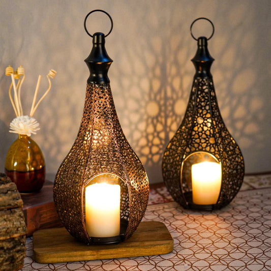 Two lit Moroccan lanterns sit on a wooden surface, casting patterned shadows on the wall behind them.