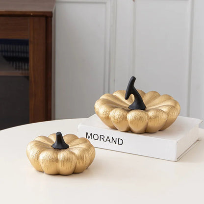 A gold decorative pumpkin with a black stem sits on a table next to a larger gold pumpkin on a book.