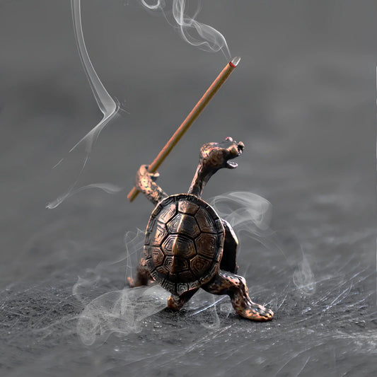 A close-up of a small, detailed bronze incense holder shaped like a turtle holding a burning incense stick like a sword, with smoke swirling around it.