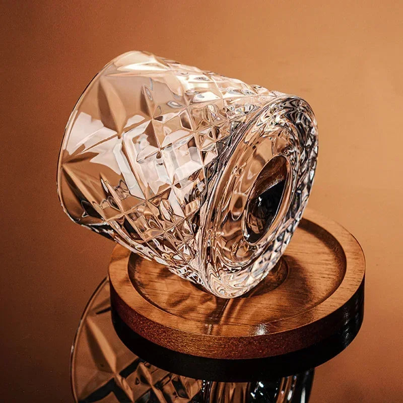 An empty, cut-crystal whiskey glass is tilted on a wooden coaster.
