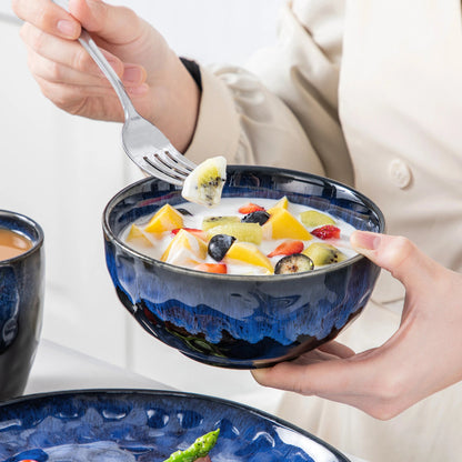 A person holds a vibrant blue bowl with yogurt and fresh fruit, with a fork poised to take a bite.