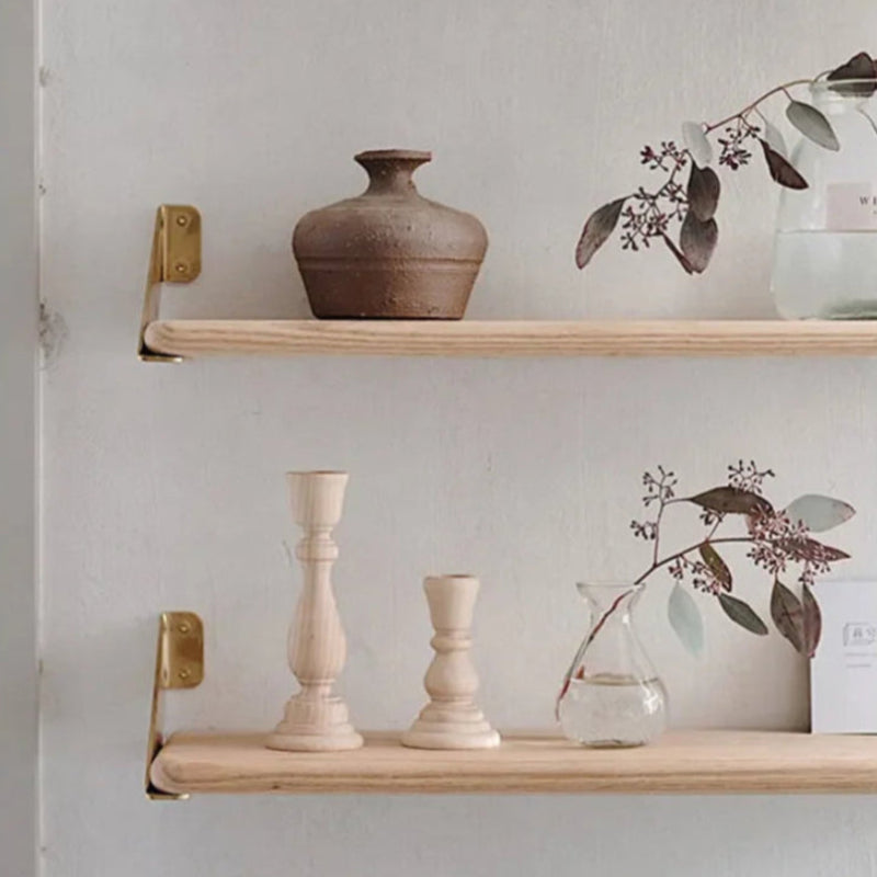 Two natural wood shelves with brass brackets hold various decorative items, including a textured brown vase, light wood candlestick holders, and glass vases with plants.