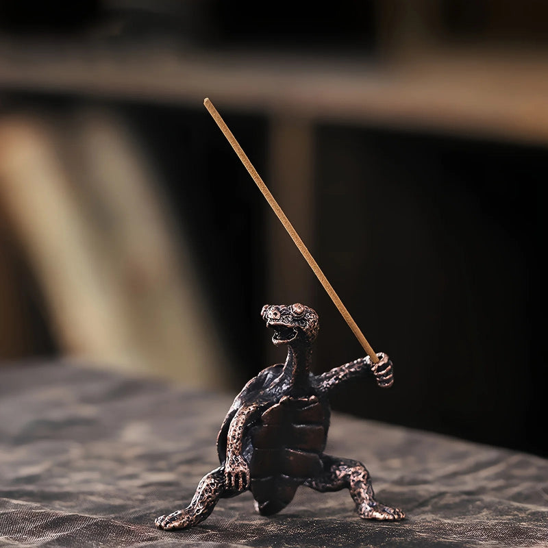 A bronze turtle incense holder holding an unlit incense stick.