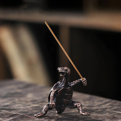 A bronze turtle incense holder holding an unlit incense stick.