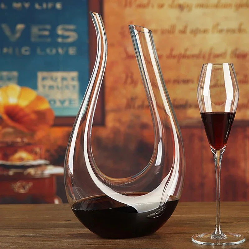 A clear, swan-shaped glass wine decanter filled with red wine, standing next to a stemmed wine glass.