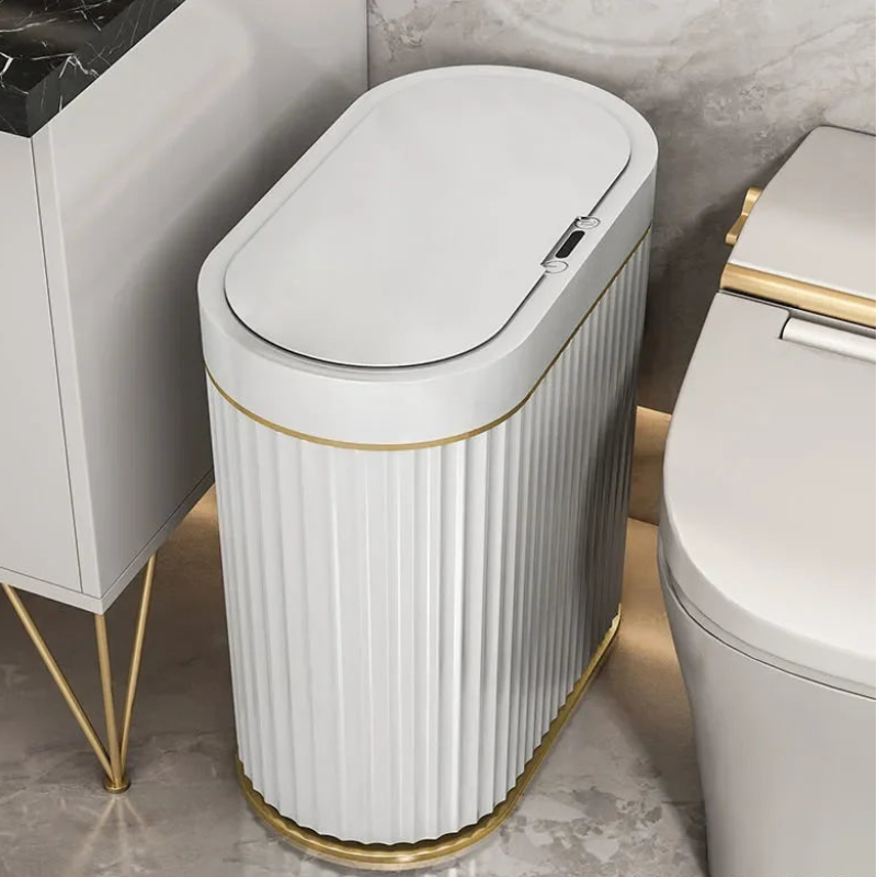 Tall, oval, white, smart trash can with vertical fluting and gold base and trim.