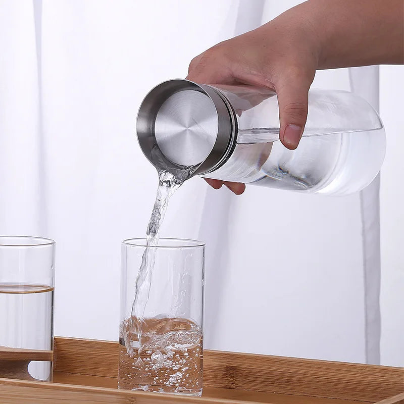 A hand pouring water from a glass carafe with a metal lid into a tall glass.