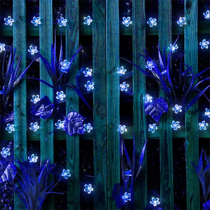Blue LED flower lights decorating a wooden fence and plants at night.