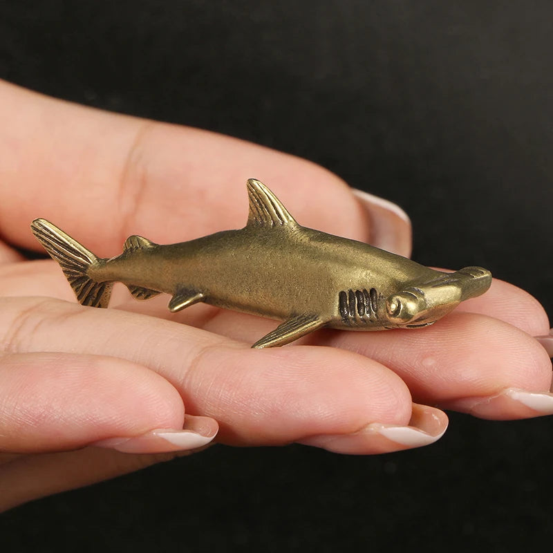 Bronze shark figurine held in a hand against a black background