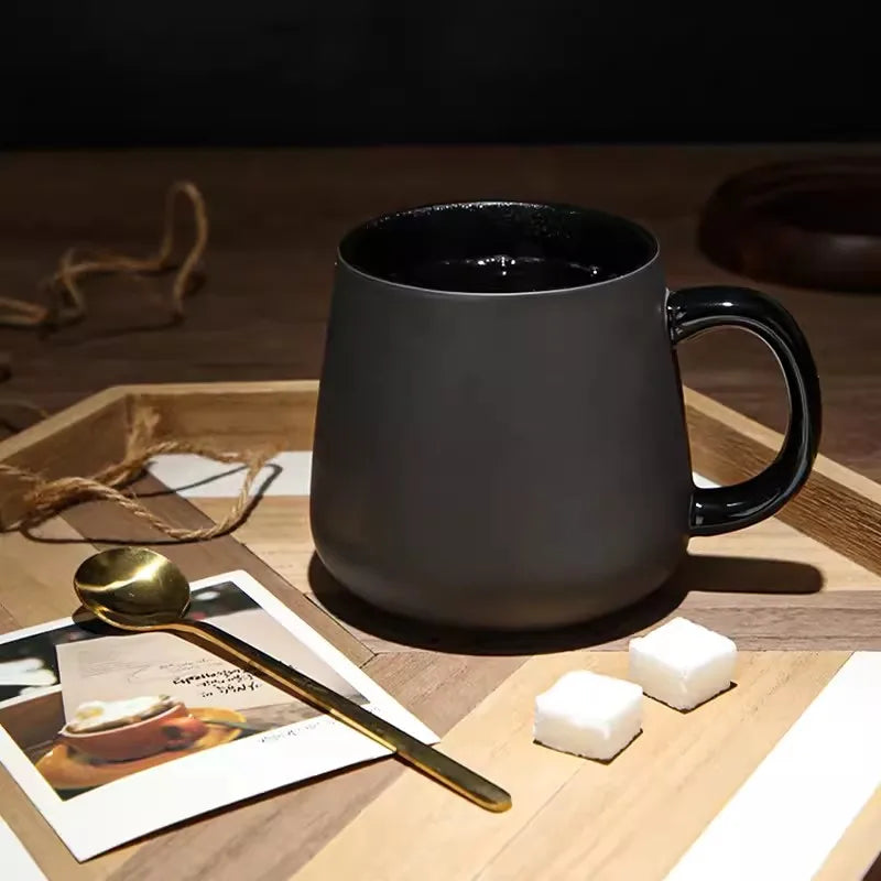 A black mug on a patterned wooden tray with a gold spoon, a photograph, and two sugar cubes.