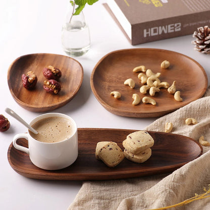 Close-up shot of an assortment of wooden serving dishes. An oval tray holds a white mug with a latte and two cookies, a small round plate holds three dates, and a larger plate holds cashews.