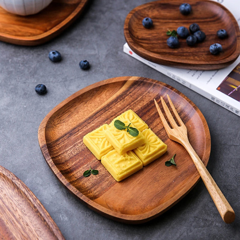 Wooden serving plate holding yellow square cookies topped with mint, beside a wooden fork. Another wooden plate with blueberries is in the background.