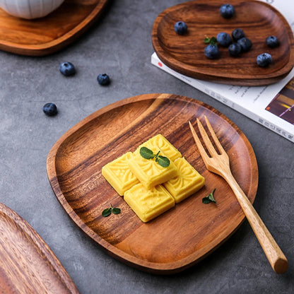 Wooden serving plate holding yellow square cookies topped with mint, beside a wooden fork. Another wooden plate with blueberries is in the background.