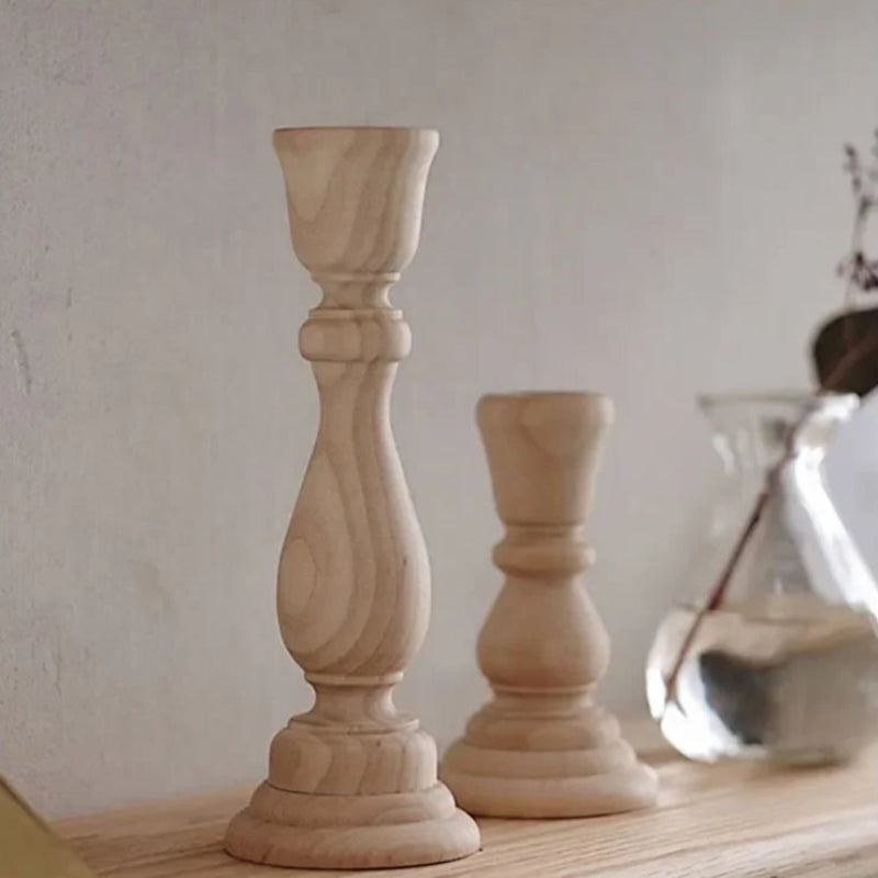 Two turned wood candlestick holders, one tall and one short, sit on a wood shelf.