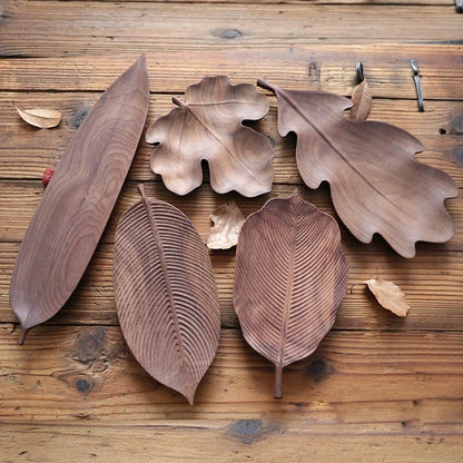 A collection of five different dark wood leaf-shaped platters arranged on a rustic wooden table.