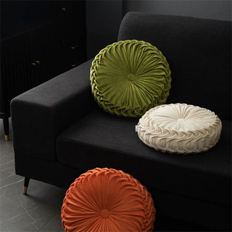 Three round textured pillows in green, white, and orange on a black sofa.