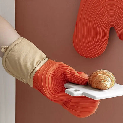 Red silicone glove holding a white tray with a croissant against a brown background