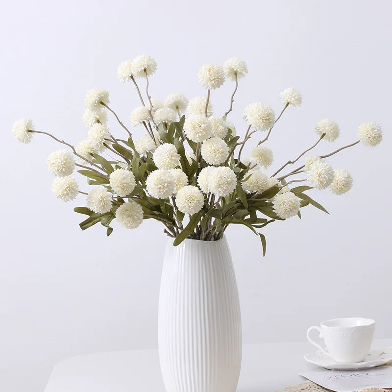 A vase holds a bouquet of white artificial dandelion-like flowers.
