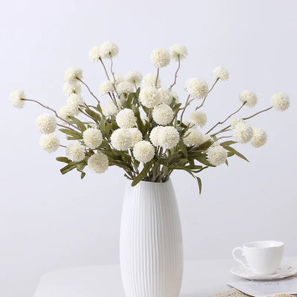 A vase holds a bouquet of white artificial dandelion-like flowers.