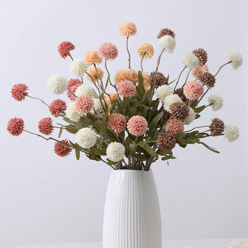 A bouquet of artificial dahlia flowers in muted pinks, whites, and browns sits in a white fluted vase.