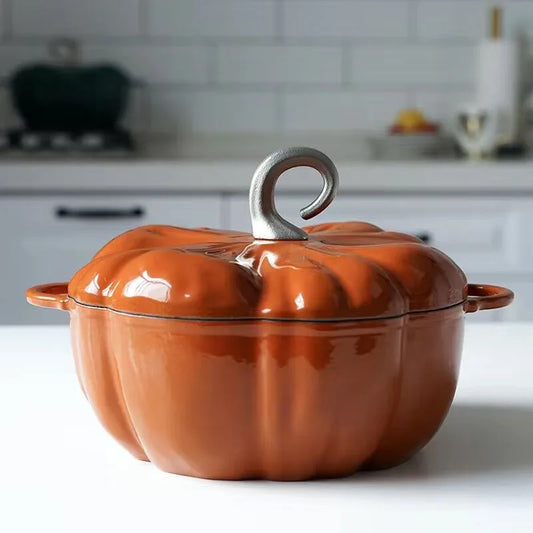 An orange, pumpkin-shaped cast iron pot with a gray stem-like handle sits on a counter.