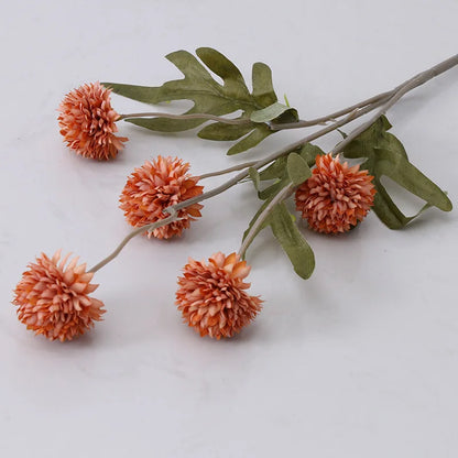 Artificial orange pompom flowers with green leaves.