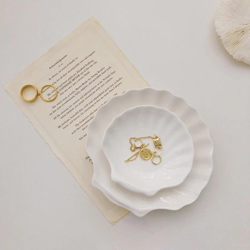 Jewelry on two shell-shaped ceramic dishes and paper.