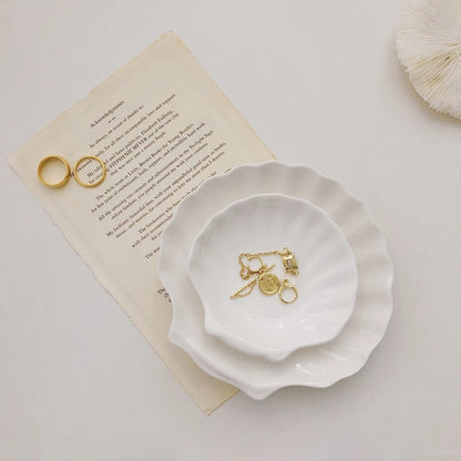 Jewelry on two shell-shaped ceramic dishes and paper.