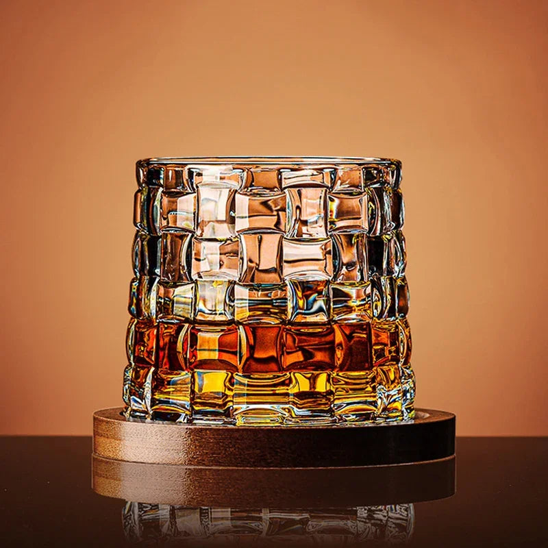 A patterned glass with a basket-weave texture, filled with amber liquid, sits on a wooden coaster.